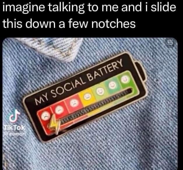 A novelty pin with a sliding gauge labeled "My Social Battery" showing a decreasing energy level while on denim.