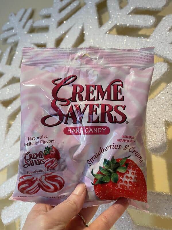 A person's hand holding a bag of the iconic red-and-white swirled Strawberries & Creme Savers hard candies.