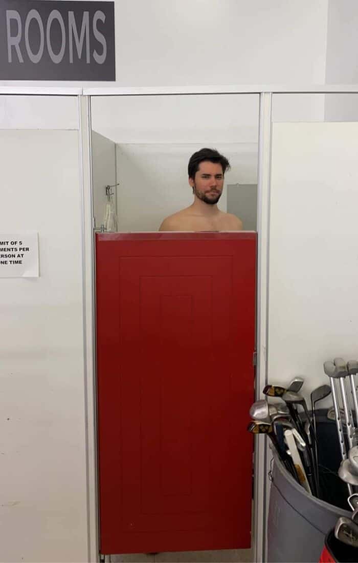 A tall people problems photo of a man staring over the top of a changing room door.