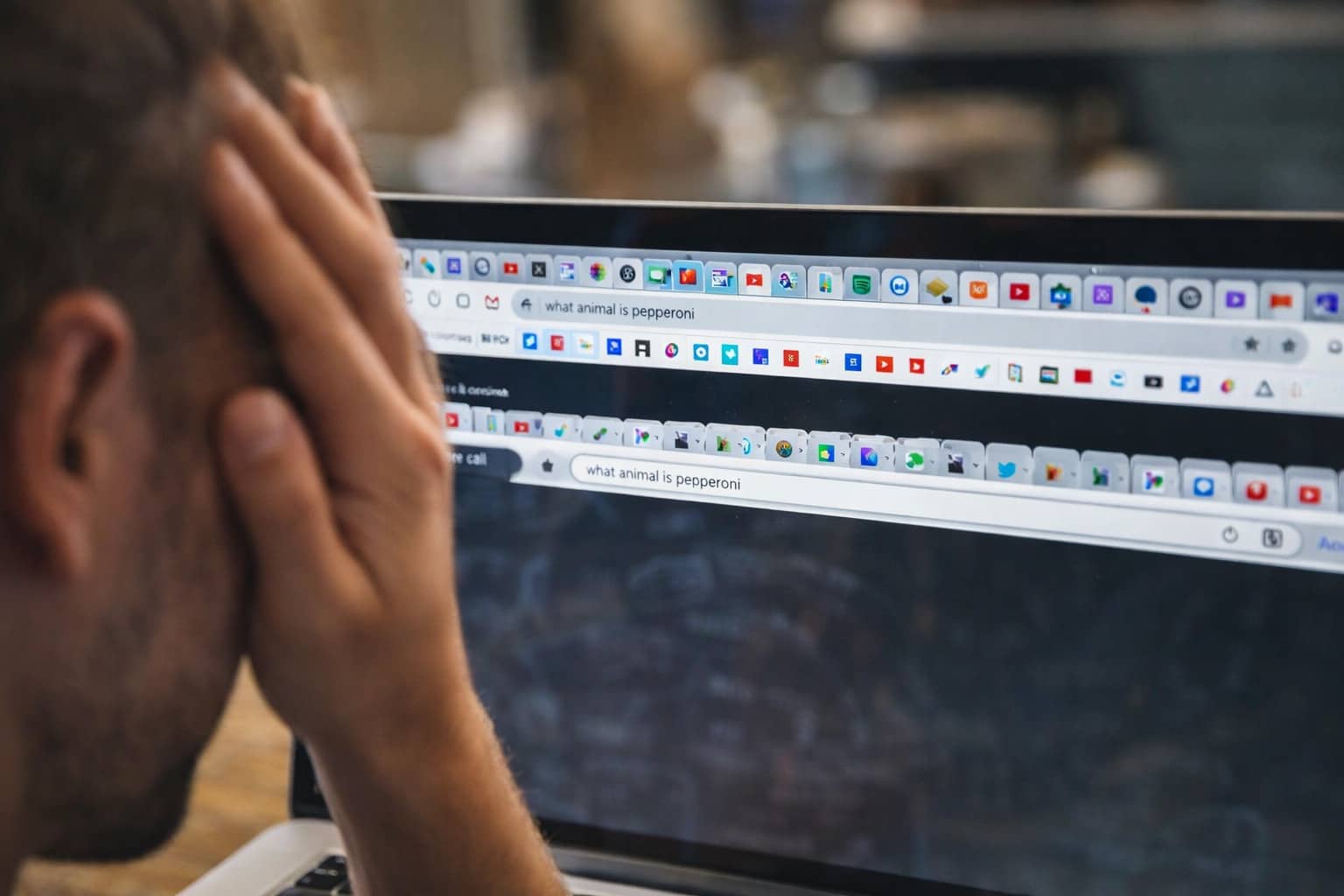 Stressed man holding his head while looking at a computer screen with too many browser tabs.