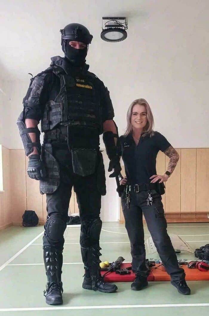 Extremely tall tactical officer in full gear standing next to a much shorter female colleague.
