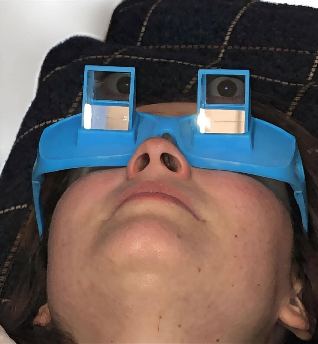 A deeply relatable and humorous classic meme showing a person lying flat on their back in bed while wearing absurd blue 90-degree prism glasses to read or watch TV without lifting their head, an iconic visual in the pantheon of lazy old memes.