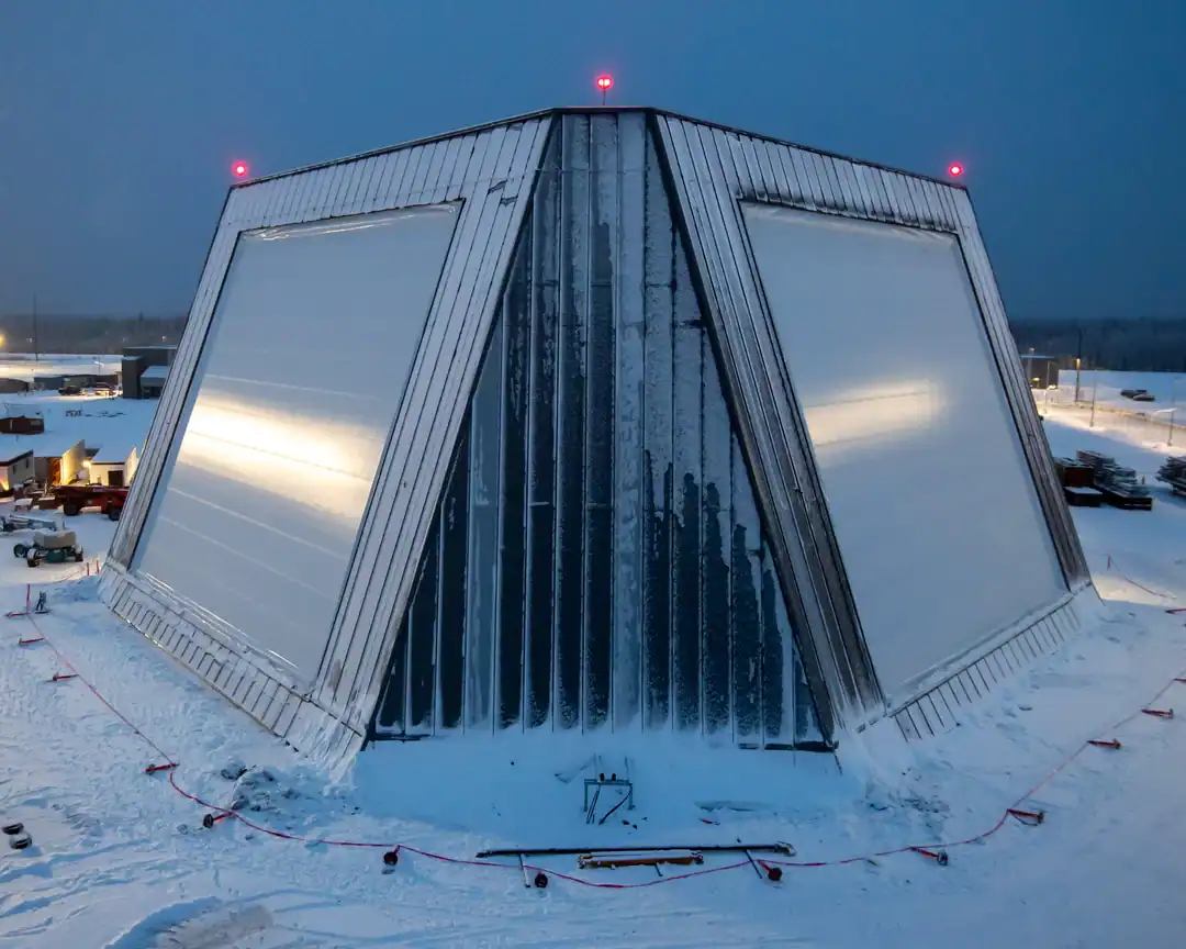 A stark geometric radar station sits isolated in a snowy landscape under red warning lights.