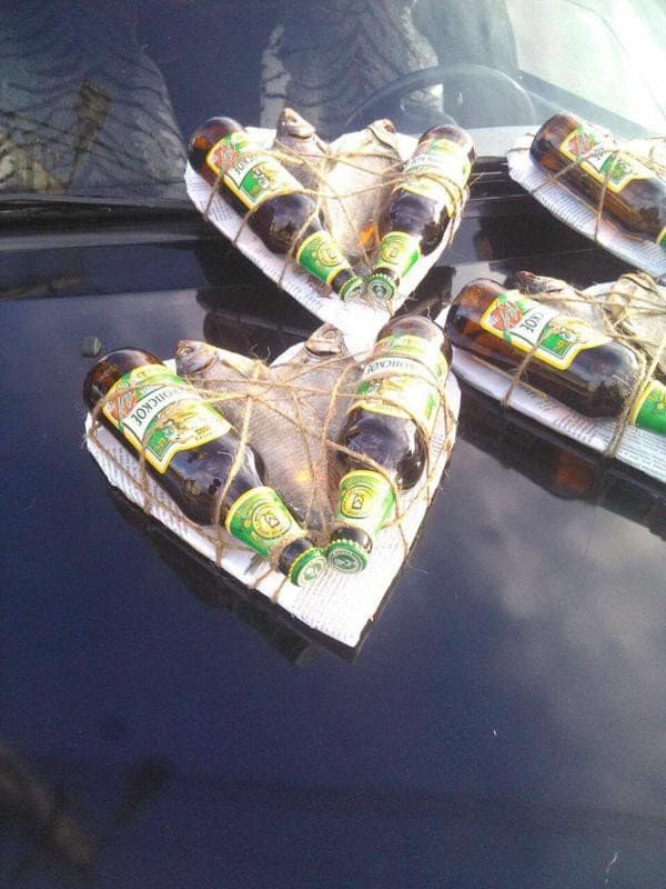 Black car hood weirdly decorated with bundles of dried fish and beer bottles on cardboard hearts in these hilarious memes.