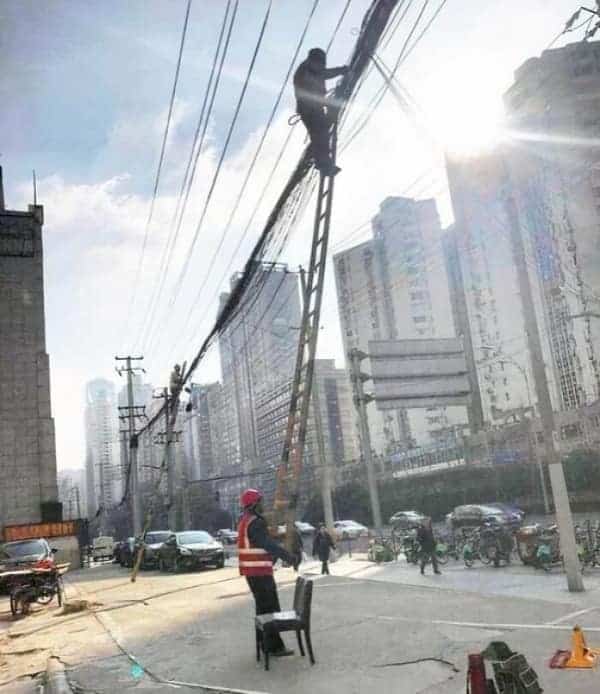 An anxiety-inducing osha meme capturing a worker high up on two ladders tied together, while a coworker on the ground uses a plastic chair to "stabilize" the base.