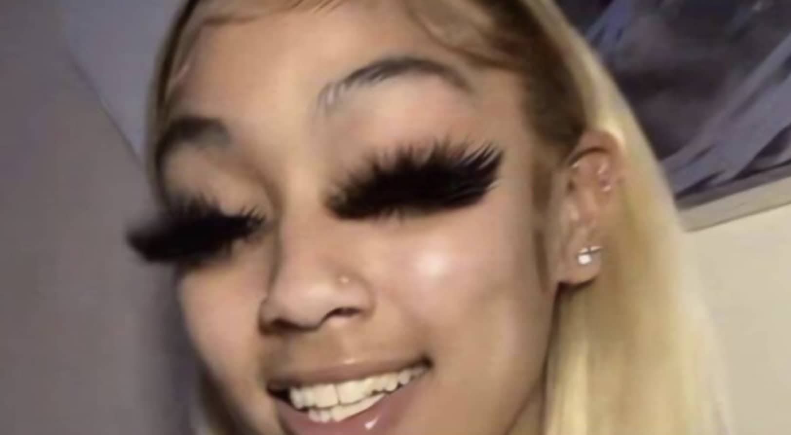 Young woman with blonde hair smiling while wearing extremely thick and oversized black eyelash extensions.