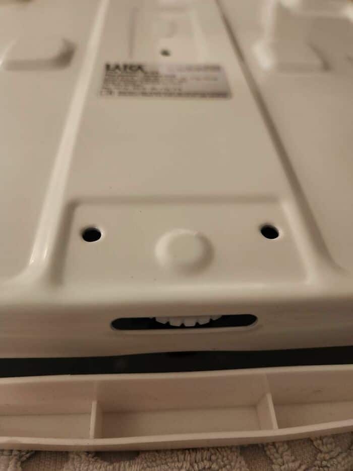 A very cute example of inanimate objects with faces found on the underside of a white plastic device, where two recessed screw holes and a small slotted opening create a cheerful, happy little face.