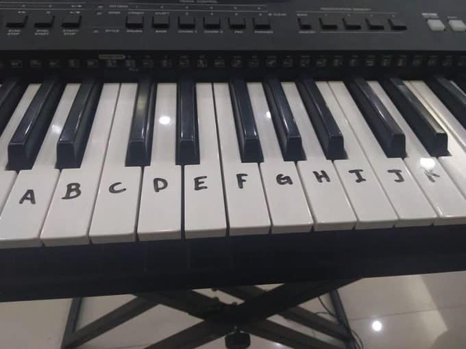 A painful cursed instrument close-up of a digital keyboard. A beginner has labeled the white keys with permanent marker, but instead of the musical scale (A-G), they have simply continued the alphabet, resulting in keys labeled H, I, J, and K.