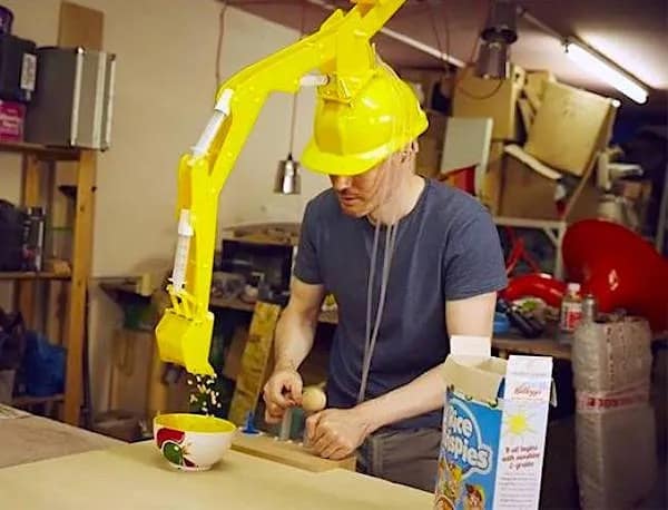 A funny meme showcasing a "useless invention": a man wearing a yellow hardhat with a fully functional, articulated miniature excavator arm attached, which he is using to scoop cereal into a bowl.