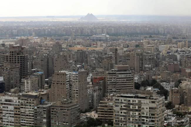 Cairo concrete urban sprawl aerial view with ancient Giza pyramids barely visible through thick haze