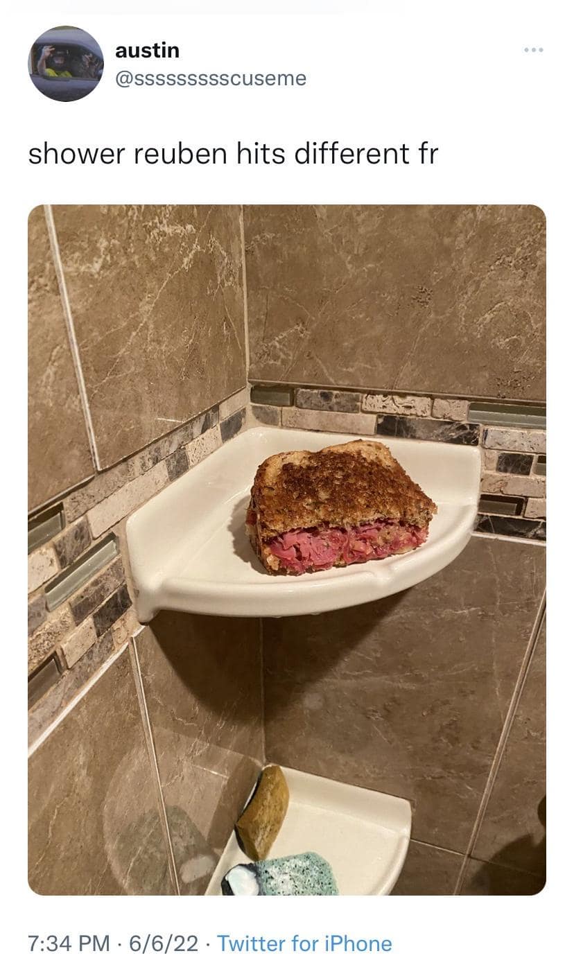A grilled corned beef Reuben sandwich loaded with pink meat and sauerkraut rests directly on a ceramic corner soap shelf inside a tiled shower stall, widely shared across this food-centric meme dump.