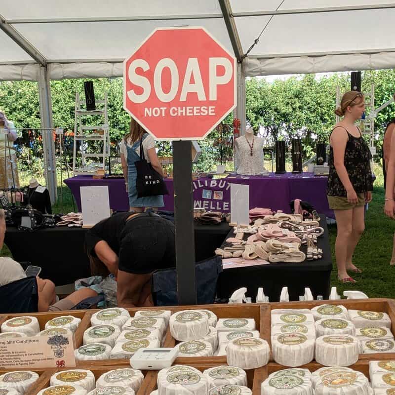 Market display of artisan soaps with a sign reading SOAP NOT CHEESE.