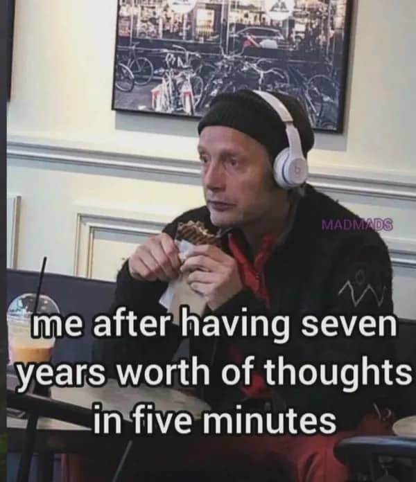 Actor Mads Mikkelsen wearing headphones in cafe looking stressed with overthinking caption, funny memes.