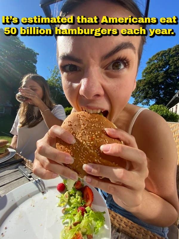 An intense, ultra-close-up perspective photo of a woman fiercely devouring a sesame seed burger, overlaid with a surprising random fact stating that Americans consume an estimated 50 billion hamburgers every year.
