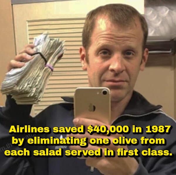 A financial corporate random fact showing Paul Lieberstein (Toby from The Office) posing with a massive stack of cash in a mirror selfie, paired with text explaining American Airlines saved $40,000 in 1987 by cutting a single olive from first-class salads.