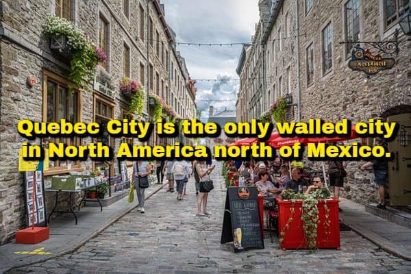 A North American historical random fact showcasing a picturesque cobblestone street in Old Quebec City with historic stone architecture and outdoor dining, highlighting that it is the only fortified walled city north of Mexico.