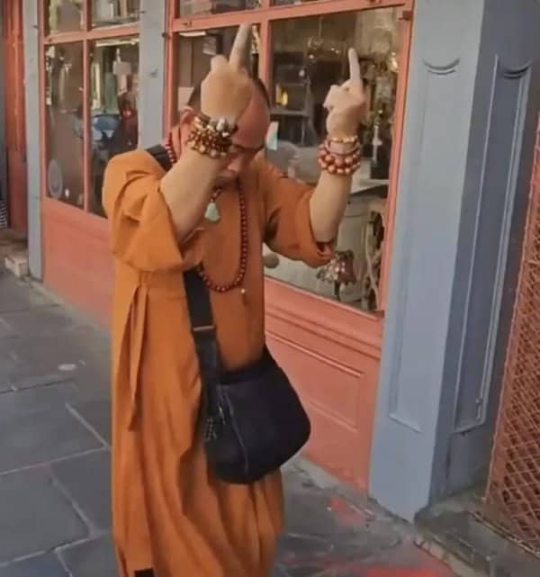 Person in orange monk robes making a rude double hand gesture on a sidewalk
