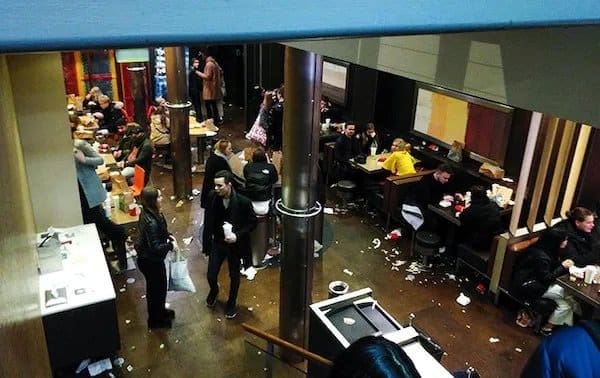 Crowded fast food restaurant with trash, napkins, and cups scattered all over the floor.