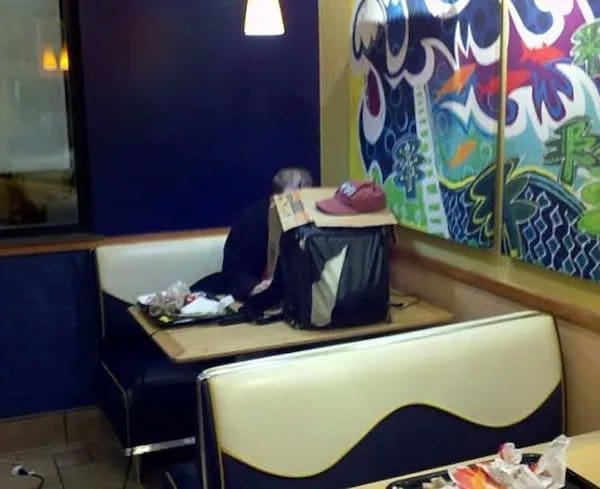 Customer asleep in a fast food booth behind a propped-up bag with a cap on top.