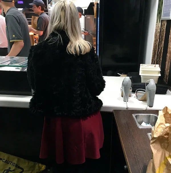 Woman at a fast food counter with her gray high heels resting on top of it.