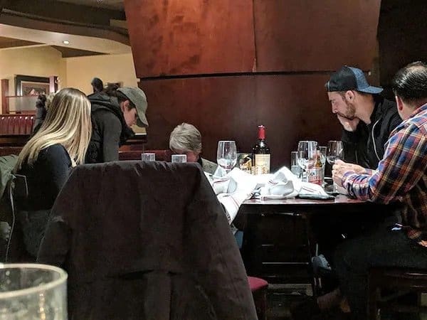 Group of diners at a restaurant table with every head bowed down toward the table.
