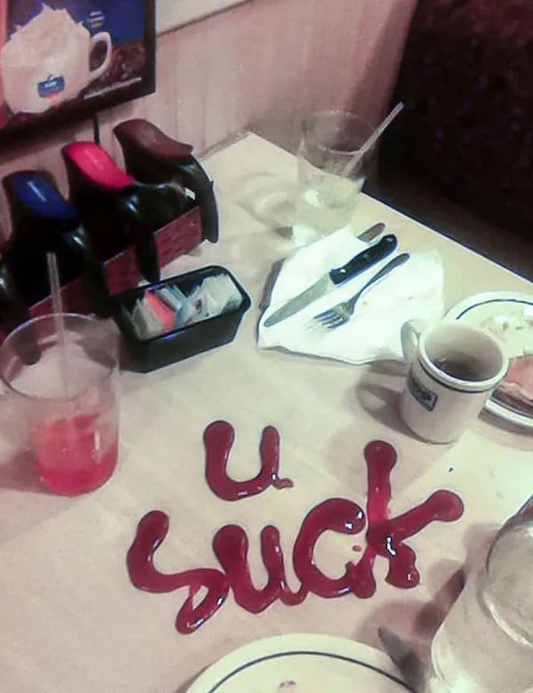 Diner table with an insult written in ketchup next to plates, cups, and coffee.
