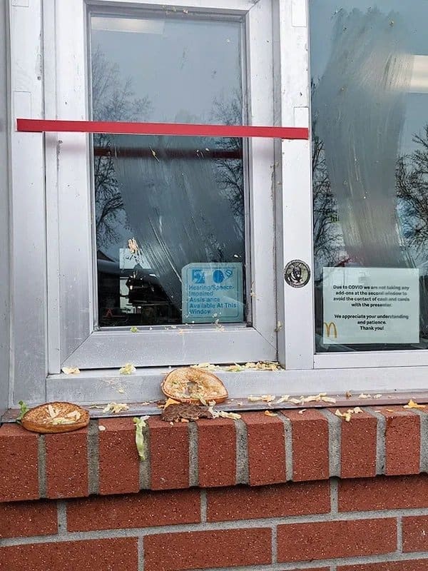 Burger thrown at a fast food drive-thru window, bun and toppings smeared across the glass.