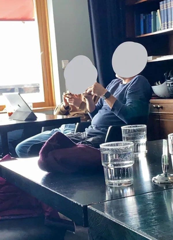 Two restaurant customers with blurred faces lounging across the chairs, absorbed in their phones.