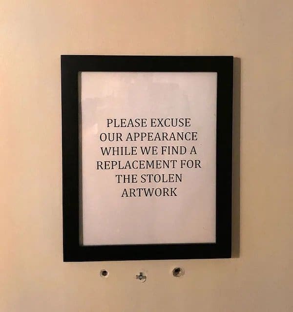 Framed sign asking guests to excuse the wall while the restaurant replaces stolen artwork.