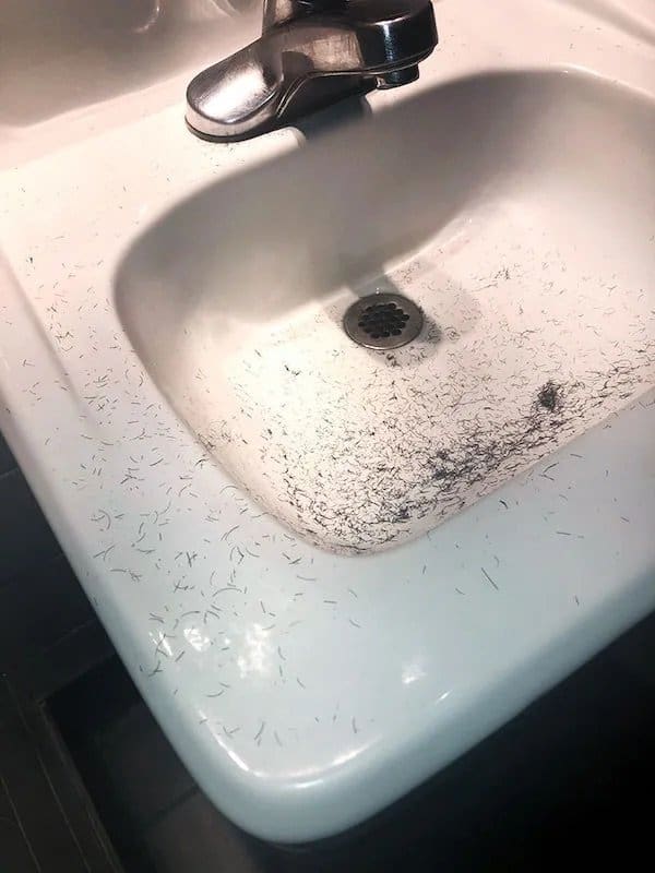 Restaurant bathroom sink covered in shaved beard hair left behind by a customer.