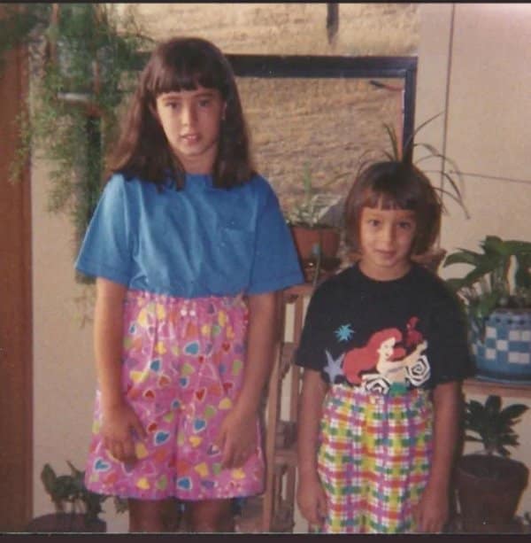 Two sisters with matching bangs in bright patterned shorts, one wearing a Little Mermaid shirt.