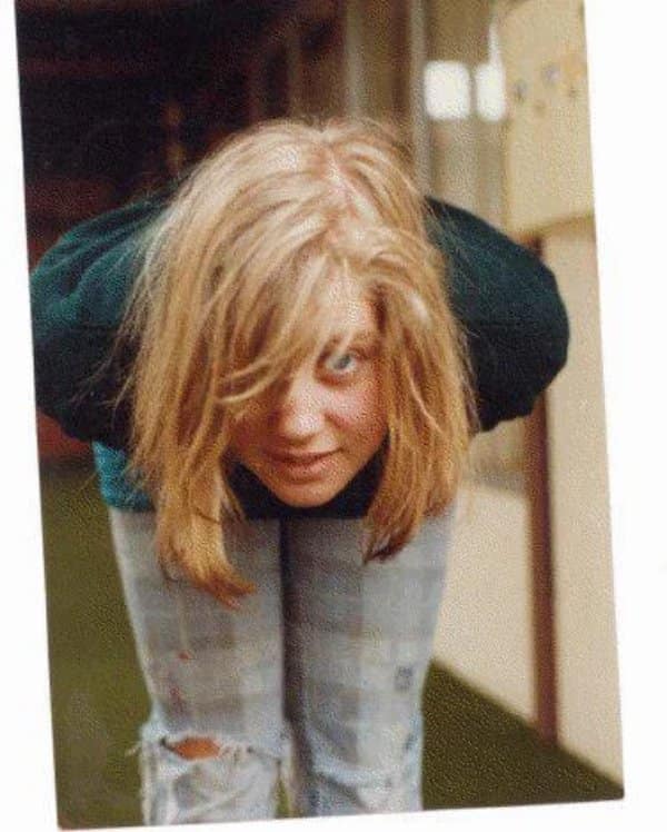 Teen leaning forward with long hair over her face and ripped jeans in a hallway.