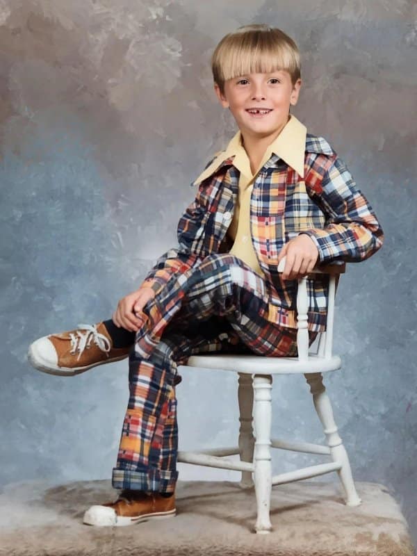 Blunder years portrait of a boy in a patchwork plaid suit posing on a chair.