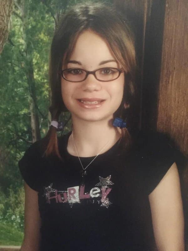Blunder years school photo of a girl with glasses, pigtails and a sparkly Hurley shirt.