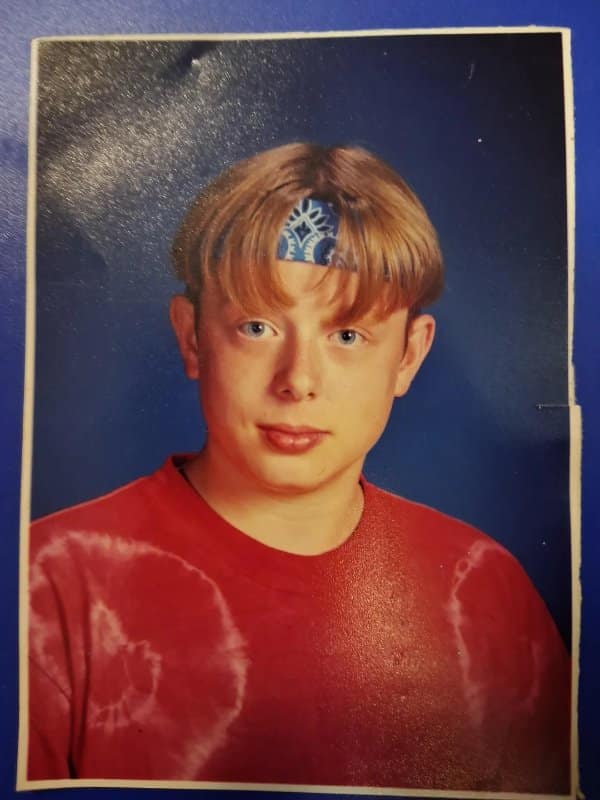 School photo of a boy with a bowl cut, bandana headband and red tie-dye shirt.