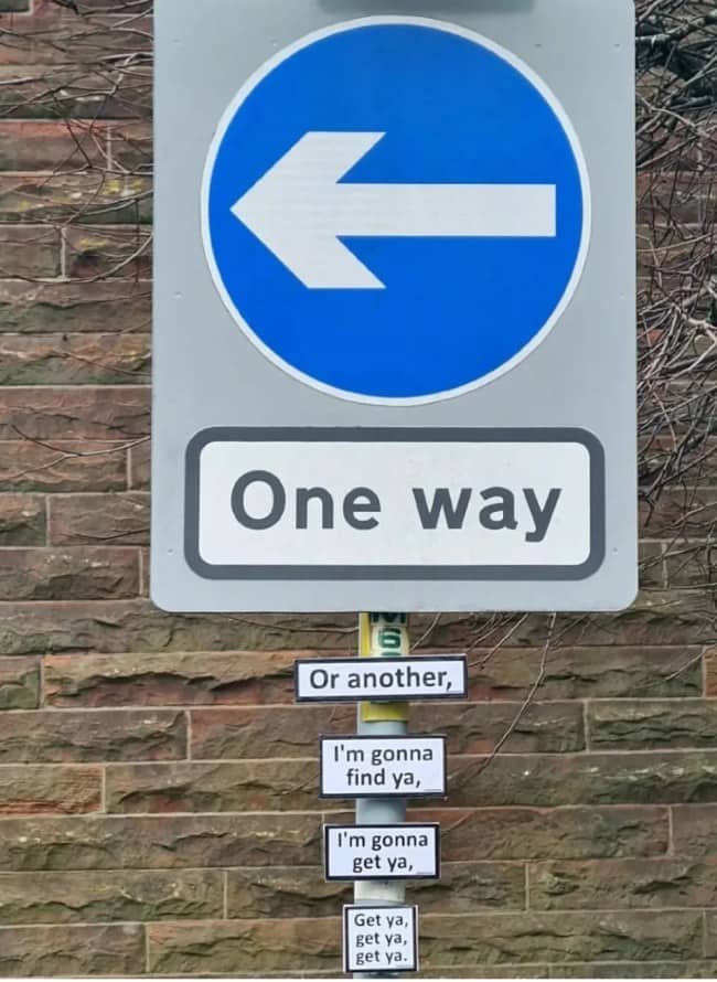 One way road sign with stickers underneath continuing a famous pop song lyric