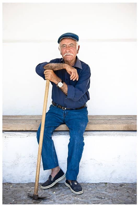 Cool grandpa with a white mustache and flat cap sitting on a bench holding a pickaxe