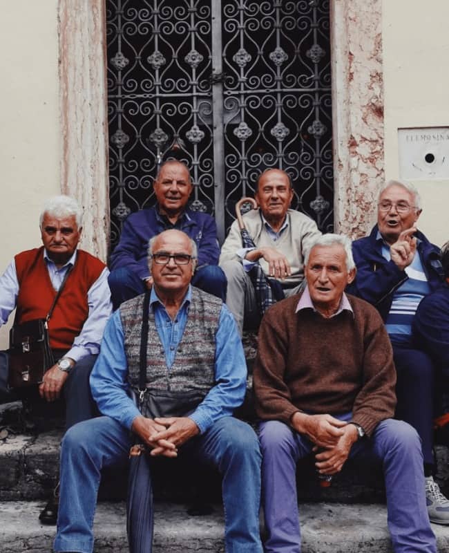 Group of older men in sweaters and vests sitting together on old church steps