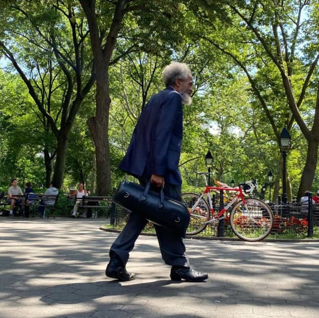 Grandpa with a white beard and navy suit walking through a park with a leather bag