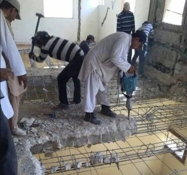 Workers jackhammering a concrete floor slab while standing on the section they are breaking.