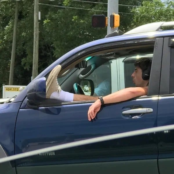 Driver resting his sneaker on the side mirror with his leg out the truck window.