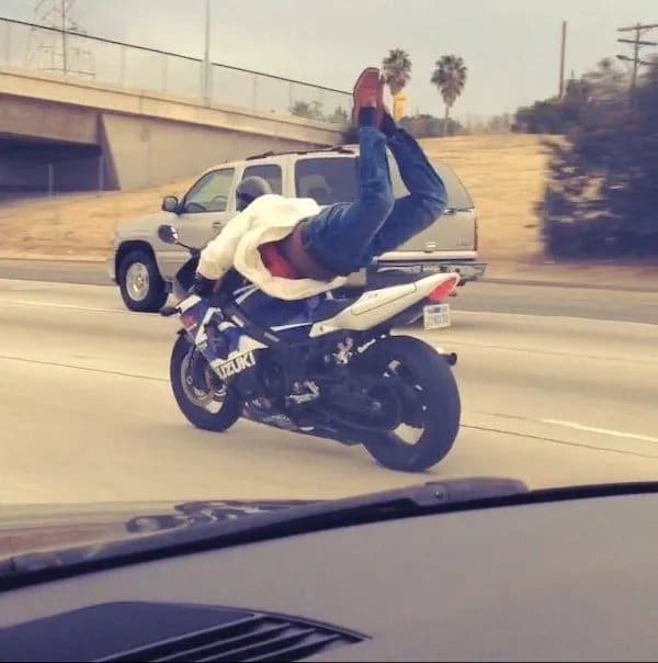 Motorcycle rider lying flat on his back with his feet in the air on a busy freeway.