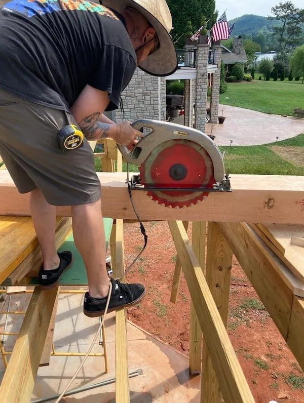 Man with a circular saw cutting the wooden beam he is standing on at a building site.