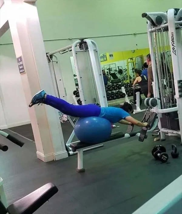 Woman balancing face down on an exercise ball stacked on a gym bench, legs raised.