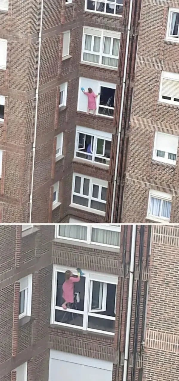 Woman in a pink robe standing on an outside window ledge high up an apartment building.