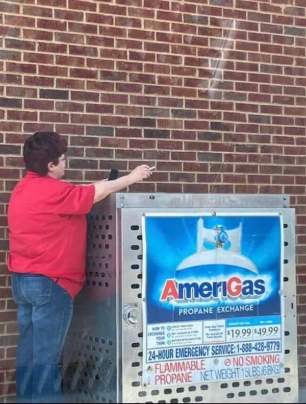 Woman lighting a cigarette right above an AmeriGas propane exchange cage marked no smoking.