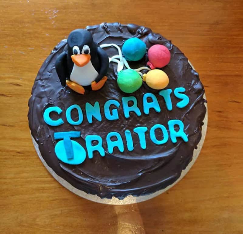 Chocolate cake with a fondant penguin and balloons spelling congrats traitor in blue letters