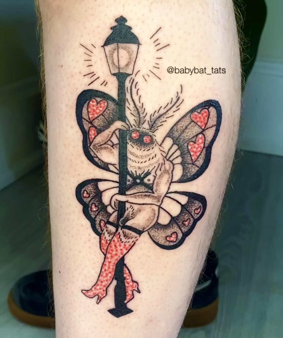Leg tattoo depicting a voluptuous moth in patterned thigh-high boots pole dancing around a street lamp in a funny meme style.