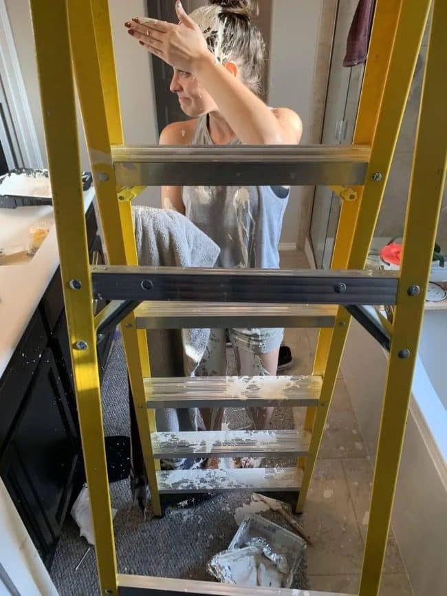 Woman covered in white paint behind a ladder after a paint tray fell on her.