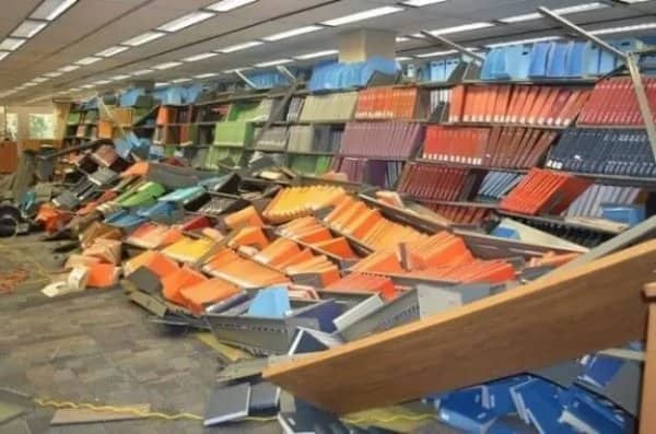 Library shelves collapsed like dominoes with colorful books scattered across the floor